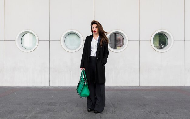 Photo gratuite femme d'affaires debout avec un sac vert à l'extérieur