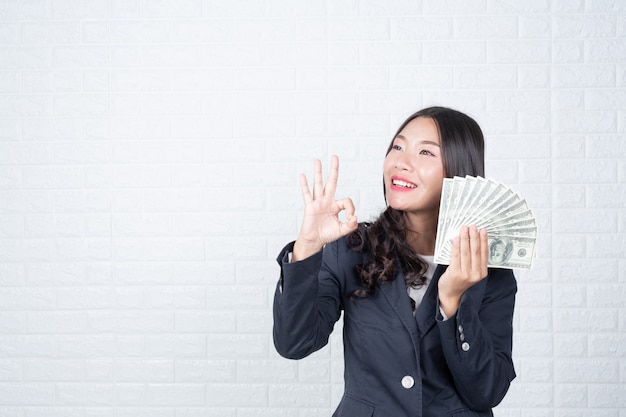 Femme d&#39;affaires détenant des billets de banque, espèces séparément, mur de briques blanches Fait des gestes avec la langue des signes.