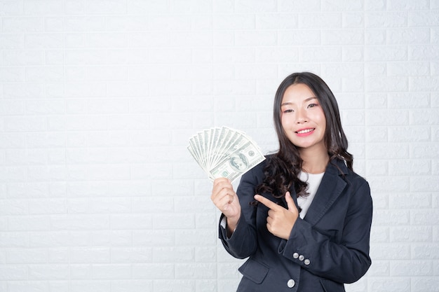 Photo gratuite femme d'affaires détenant des billets de banque, espèces séparément, mur de briques blanches fait des gestes avec la langue des signes.