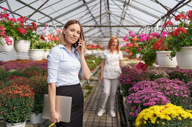 Femme d'affaires discutant au téléphone d'une proposition. Elle tient un ordinateur portable dans une maison verte avec des fleurs.