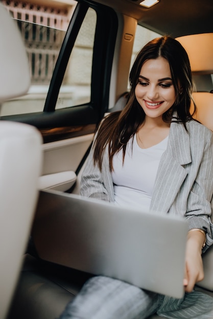 Femme d'affaires élégante assis dans la voiture et travaillant sur ordinateur portable