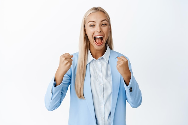 Femme d'affaires enthousiaste acclamant le chant et encourageant l'équipe à la recherche de cris motivés et excités de réalisation debout sur fond blanc