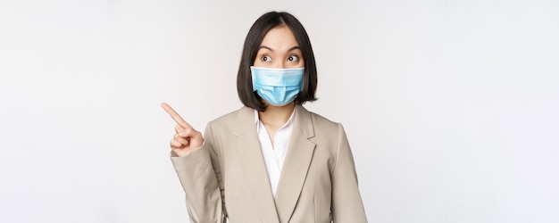 Femme d'affaires enthousiaste pointant les doigts vers la gauche portant un masque médical du stand pandémique covid