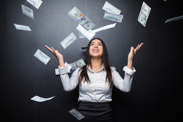 Femme d'affaires heureuse sous une pluie d'argent en dollars isolé sur un mur noir