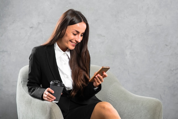 Femme d&#39;affaires heureux tenant une tasse de café jetable en regardant téléphone portable