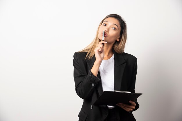 Femme d'affaires jeune debout avec son presse-papiers sur un mur blanc.