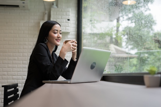 Femme d&#39;affaires jeune faire une pause avec du café tout en travaillant sur ordinateur portable au bureau