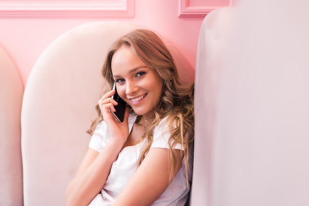 Femme D'affaires Jeune En Robe Grise, Assis à Table Dans Un Café, Parler Téléphone Portable Tout En Prenant Des Notes Dans Le Cahier Sur Ordinateur Portable De Table Et Tasse De Café. Apprentissage Des élèves En Ligne. Freelance Travaillant En Ligne.