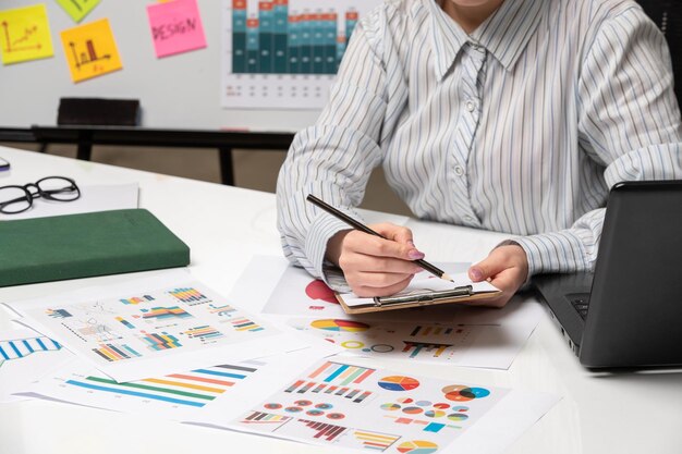 Femme d'affaires marketing en blazer gris au bureau avec ordinateur bouchent des notes d'écriture