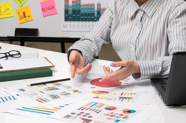 Femme d'affaires marketing en blazer gris au bureau avec ordinateur en gros plan pointant vers les graphiques