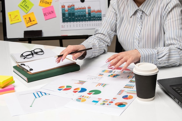 Femme d'affaires marketing en chemise rayée au bureau avec des lunettes sur le bureau travaillant avec une tasse de café