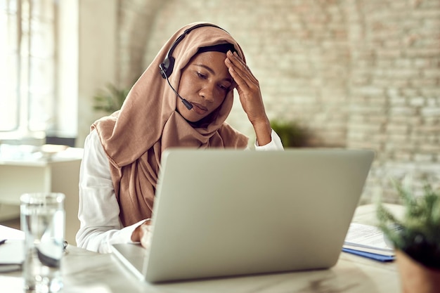 Femme d'affaires musulmane désemparée ayant mal à la tête tout en travaillant sur un ordinateur portable au bureau