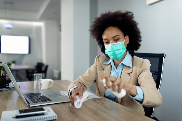 Femme d'affaires noire désinfectant la table de bureau pendant la pandémie de coronavirus