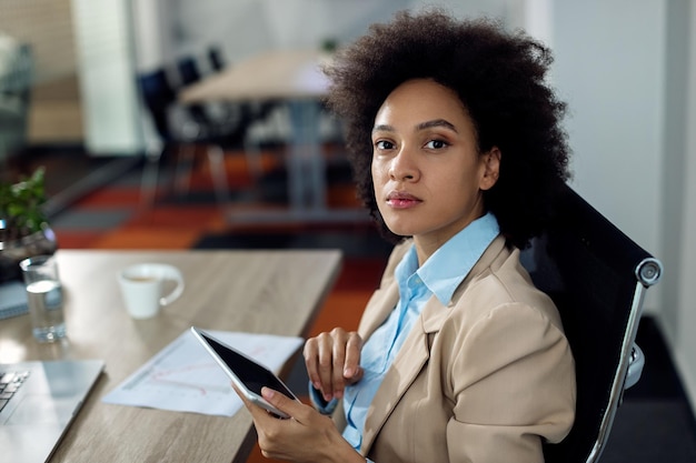 Photo gratuite femme d'affaires noire travaillant sur une tablette numérique au bureau et regardant la caméra