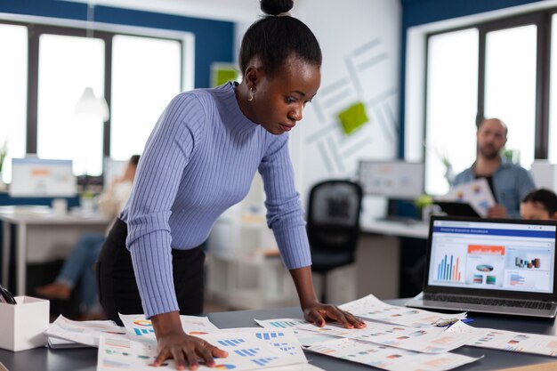 Femme d'affaires noire vérifiant le travail de collègues multiethniques dans une agence de démarrage. Équipe diversifiée d'hommes d'affaires analysant les rapports financiers de l'entreprise à partir d'un ordinateur. Start up Profession d'entreprise réussie