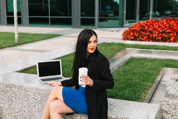 Femme d&#39;affaires avec ordinateur portable et coupe d&#39;élimination assis à l&#39;extérieur de l&#39;immeuble de bureaux