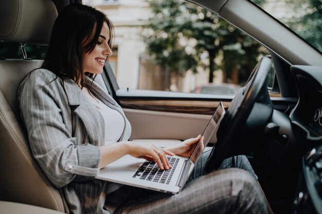 Femme d'affaires avec un ordinateur portable dans sa voiture dans la rue