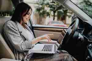 Photo gratuite femme d'affaires avec un ordinateur portable dans sa voiture dans la rue