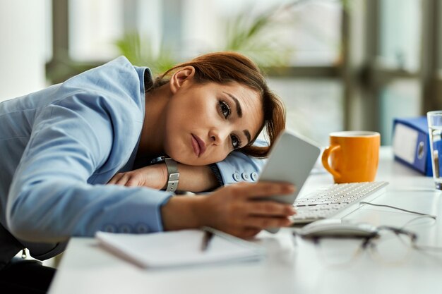 Femme d'affaires pensive utilisant un téléphone portable tout en se relaxant au bureau