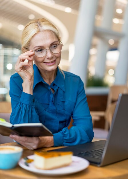 Femme d'affaires plus âgée avec des lunettes tenant l'ordre du jour et regardant un ordinateur portable