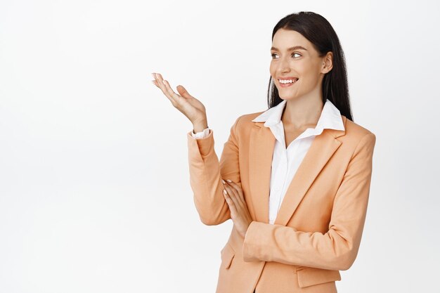 Femme d'affaires pointant sur quelque chose Vendeuse démontrant la marque sur un espace vide debout sur fond blanc