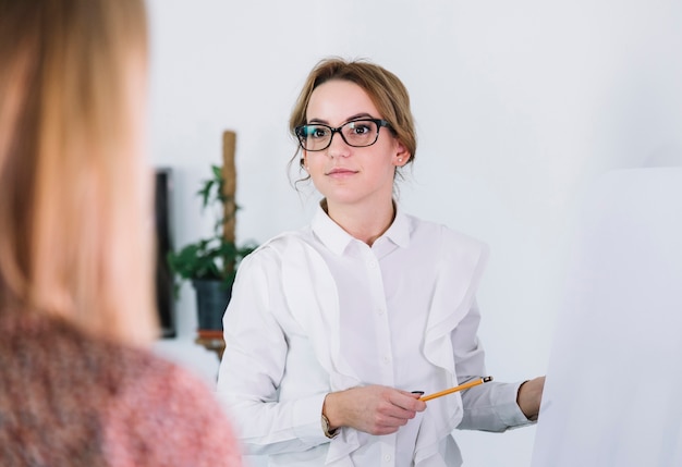 Femme d&#39;affaires pointant sur un tableau blanc tout en présentant ses idées à des partenaires commerciaux