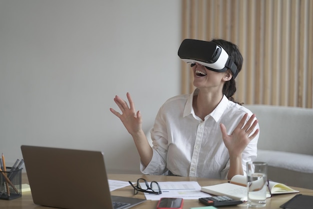 Une femme d'affaires porte un casque vr pour ordinateur portable levant les mains pour essayer de toucher des objets en réalité