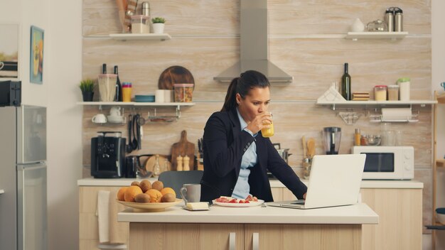 Femme d'affaires prenant son petit déjeuner et travaillant sur ordinateur portable. Femme d'affaires concentrée le matin multitâche dans la cuisine avant d'aller au bureau, mode de vie stressant, carrière et objectifs à atteindre