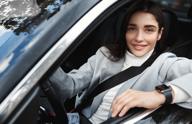 Femme d'affaires prospère conduisant sa voiture au travail, portant la ceinture de sécurité et des vêtements de cérémonie