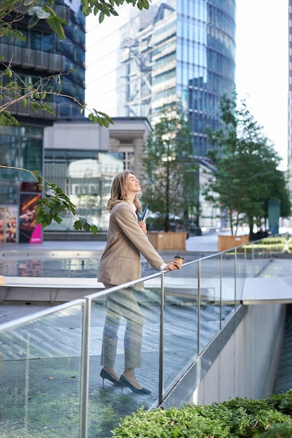 Photo gratuite femme d'affaires prospère en costume beige debout dans le centre-ville près des gratte-ciel et des bureaux