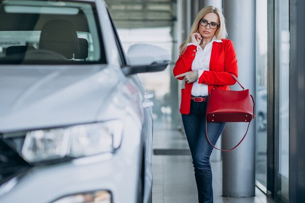 Femme d'affaires à la recherche d'un mobile auto dans une salle d'exposition de voitures