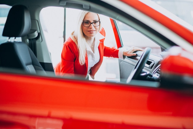 Femme d'affaires à la recherche d'un mobile auto dans une salle d'exposition de voitures