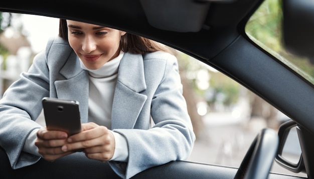 Femme d'affaires s'appuyant sur la fenêtre de la voiture et un message texte sur le téléphone, souriant heureux.