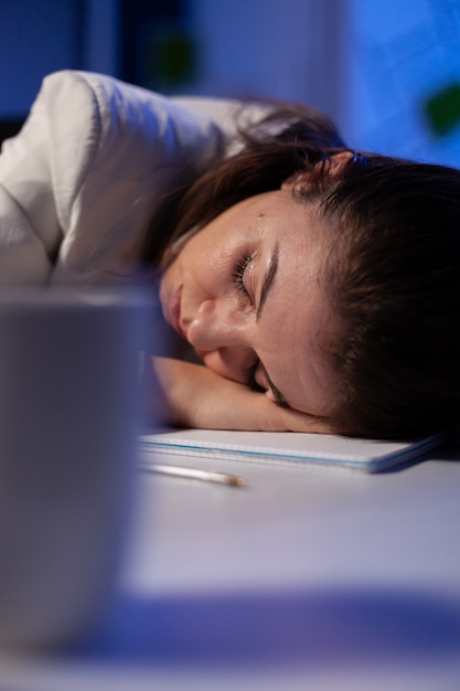 Femme d'affaires s'endormant en travaillant aux statistiques économiques tard dans la nuit dans une entreprise de bureau