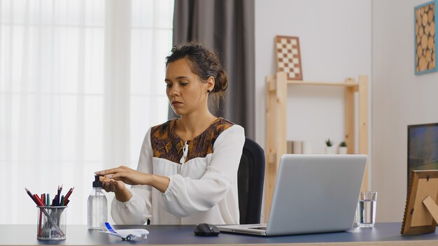 Femme d'affaires se lavant les mains avec un désinfectant tout en travaillant à domicile.