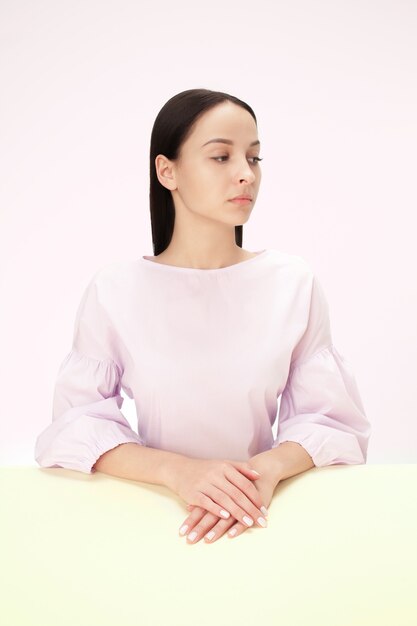 Femme d'affaires sérieuse assise à table sur un fond de studio rose. Le portrait dans un style minimalisme