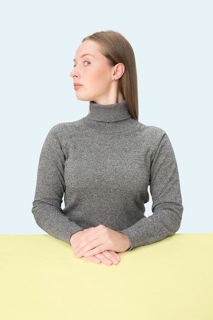 Femme d'affaires sérieuse assise à table sur un fond de studio rose.