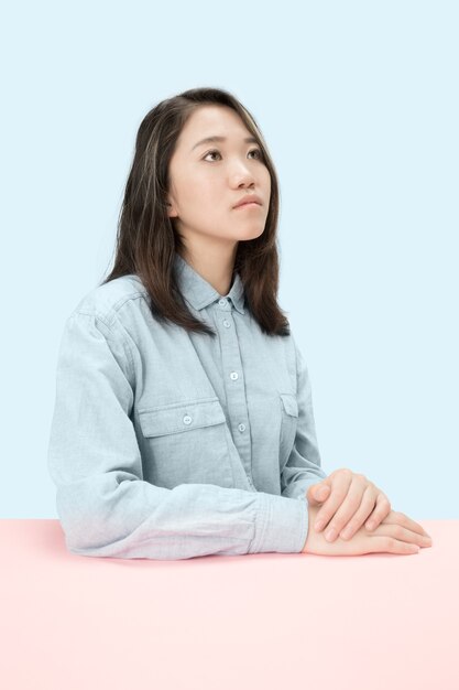 Femme d'affaires sérieuse assise à table, levant isolé sur fond de studio bleu à la mode. Portrait de femme demi-longueur.