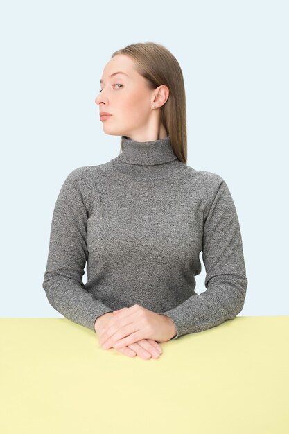 Femme d'affaires sérieuse assise à table sur un studio rose.