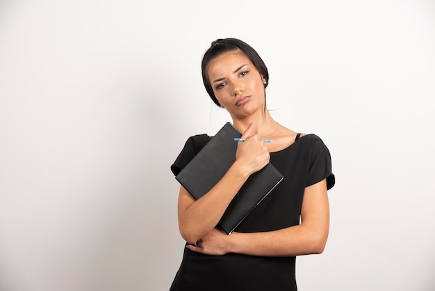 Femme d'affaires sérieuse avec ordinateur portable posant sur un mur blanc.