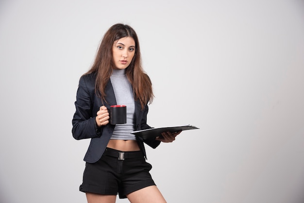 Femme d'affaires sérieuse avec une tasse et un presse-papiers.