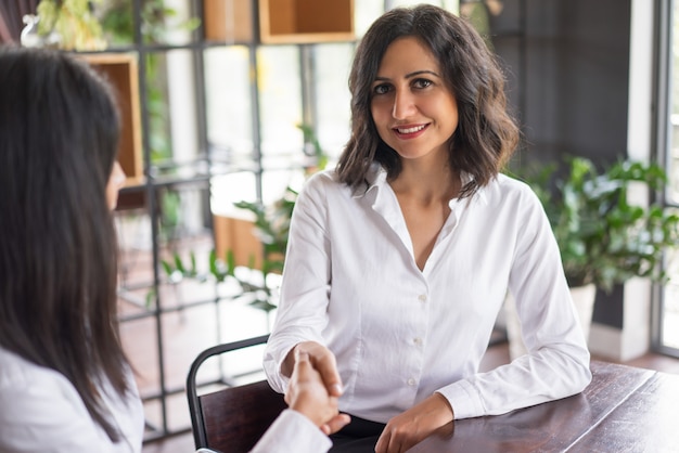 Femme d&#39;affaires souriant se serrant la main avec un partenaire au café.