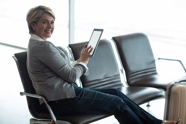 Femme d'affaires souriante à l'aide de tablette numérique dans la zone d'attente