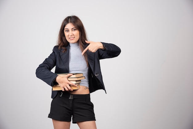 Femme d'affaires souriante pointant sur une pile de livres.