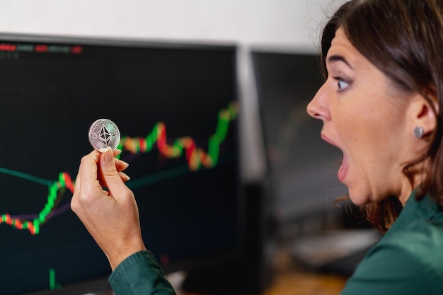 Femme d'affaires surprise tenant et regardant une pièce d'ethereum. concept de trading en ligne, d'argent virtuel et de crypto-monnaie