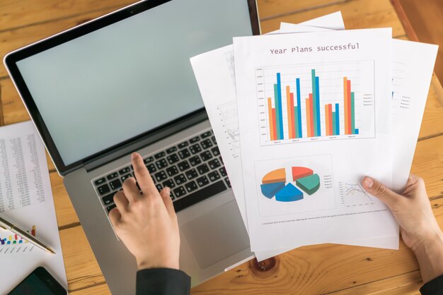 Femme d&#39;affaires avec des tableaux financiers et un ordinateur portable sur la table.