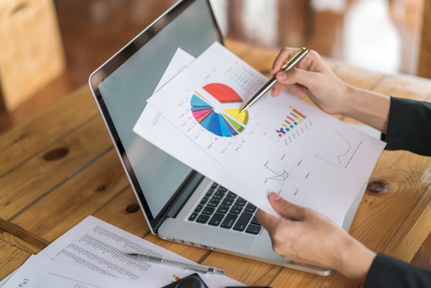 Photo gratuite femme d'affaires avec des tableaux financiers et un ordinateur portable sur la table.