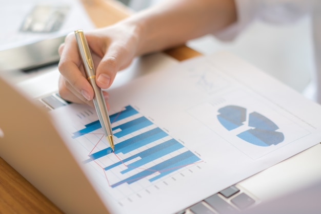 Femme d&#39;affaires avec des tableaux financiers et un ordinateur portable sur la table.