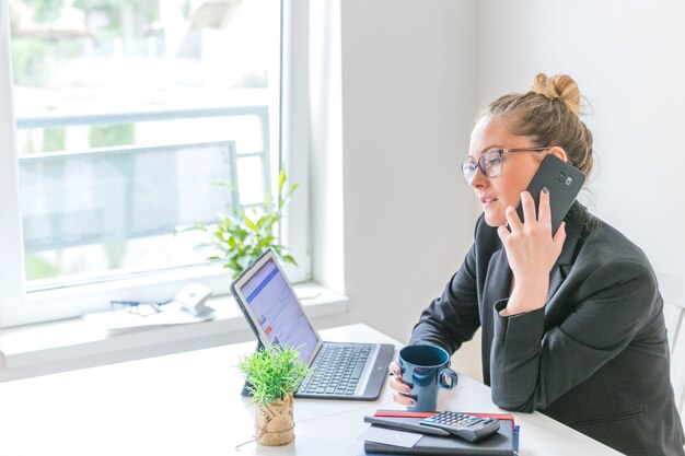 Femme affaires, à, tasse café, conversation téléphone portable, dans bureau