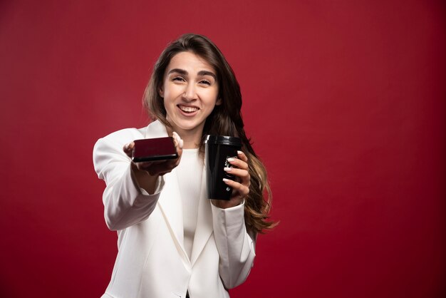 Femme d'affaires avec une tasse de café offrant un téléphone